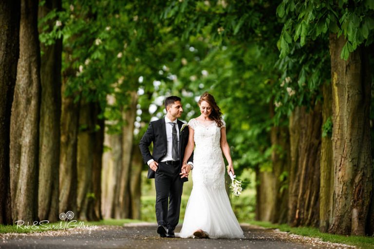 Bride and groom walking through trees at Hogarths Solihull