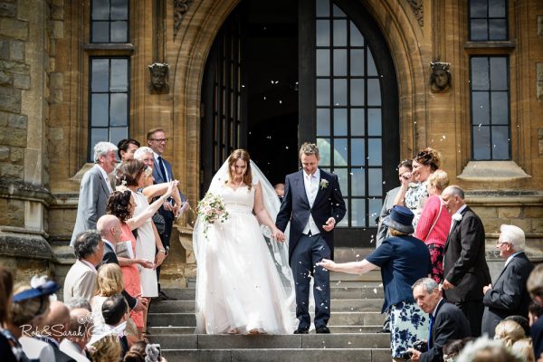 Bride and groom walk down steps as wedding guests throw confetti