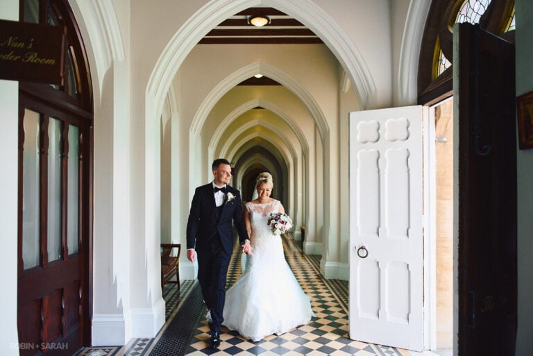 Bride and groom walk through arched corridor at Stanbrook Abbey