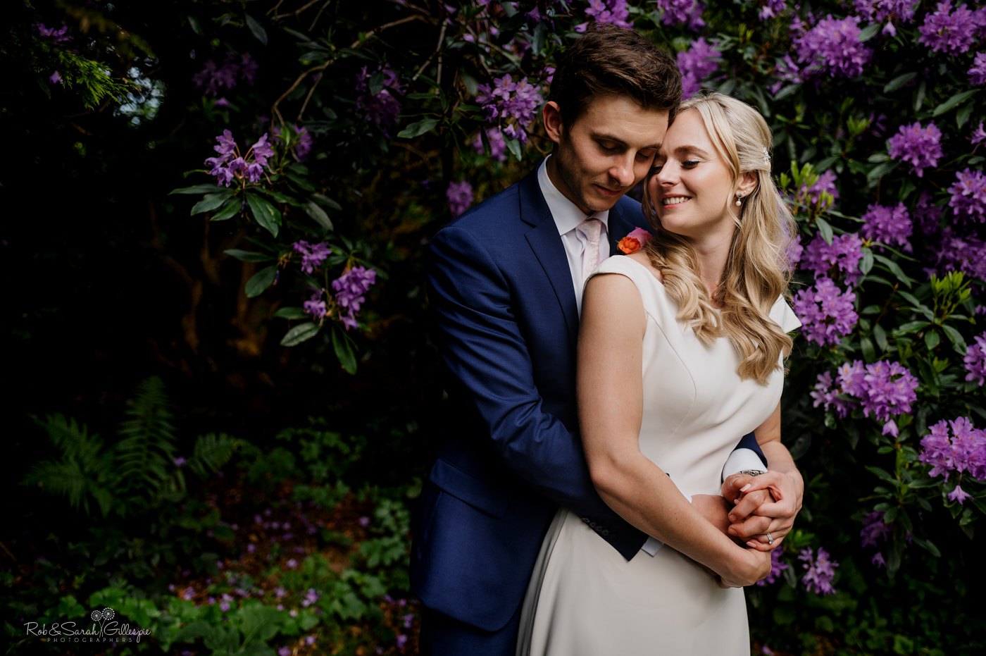 Bride and groom cuddle up surrounded by purple flowers