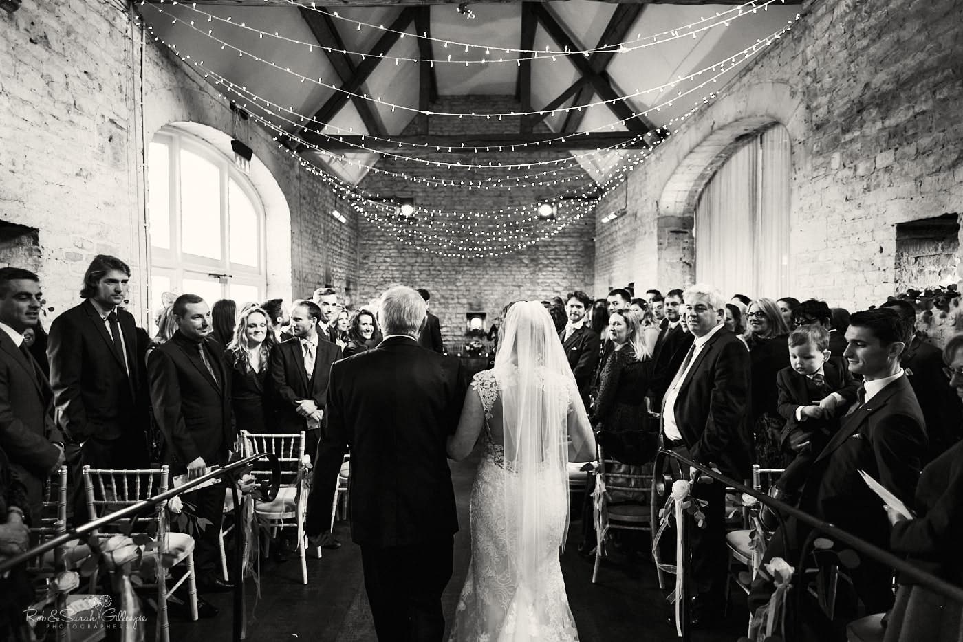 Bride and father walk up aisle as wedding guests watch