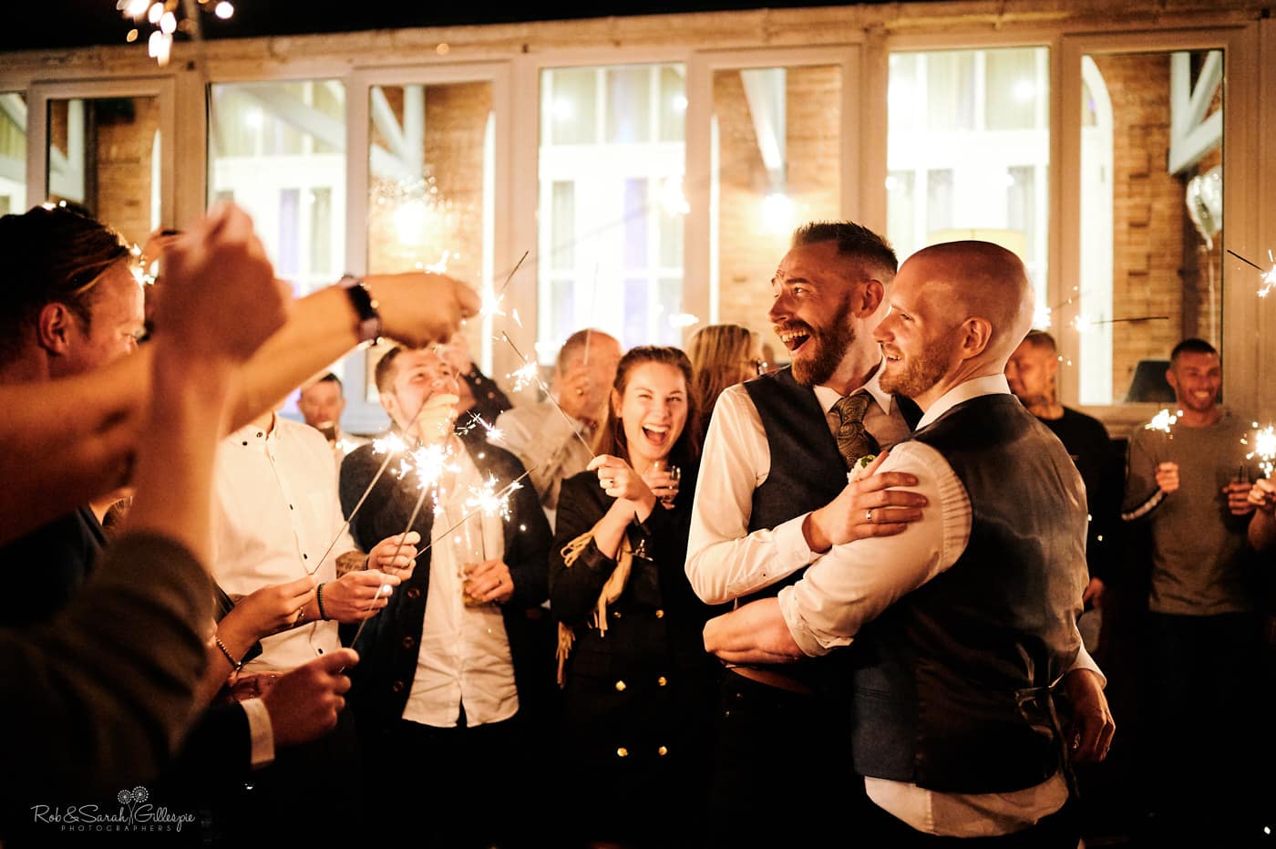 Two grooms surrounded by wedding guests with sparklers at Moor Hall Hotel