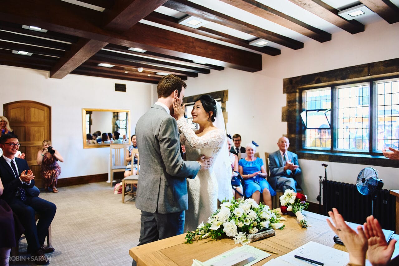 Bride strokes groom's face during wedding ceremony at The Henley Room