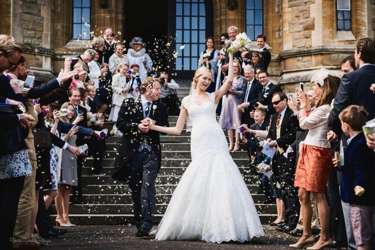 Bride and groom walk down steps as guests throw confetti