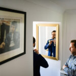 Groom adjusts tie in mirror as dad watches
