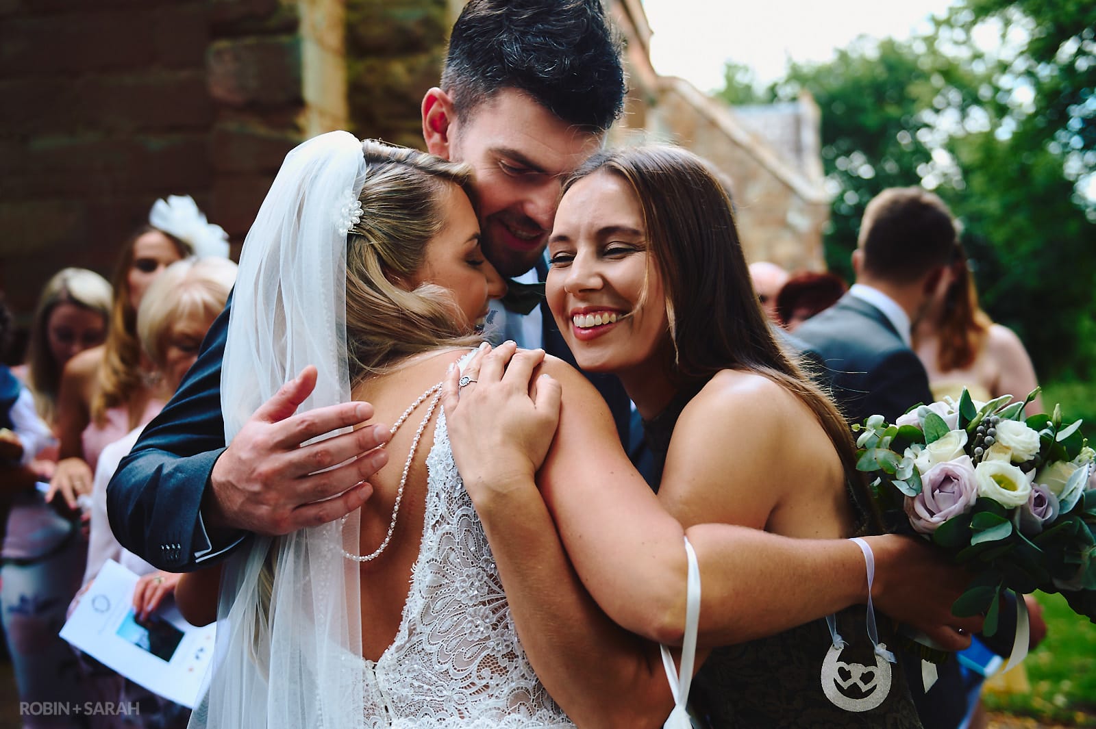 Bride hugged by two wedding guests after church ceremony