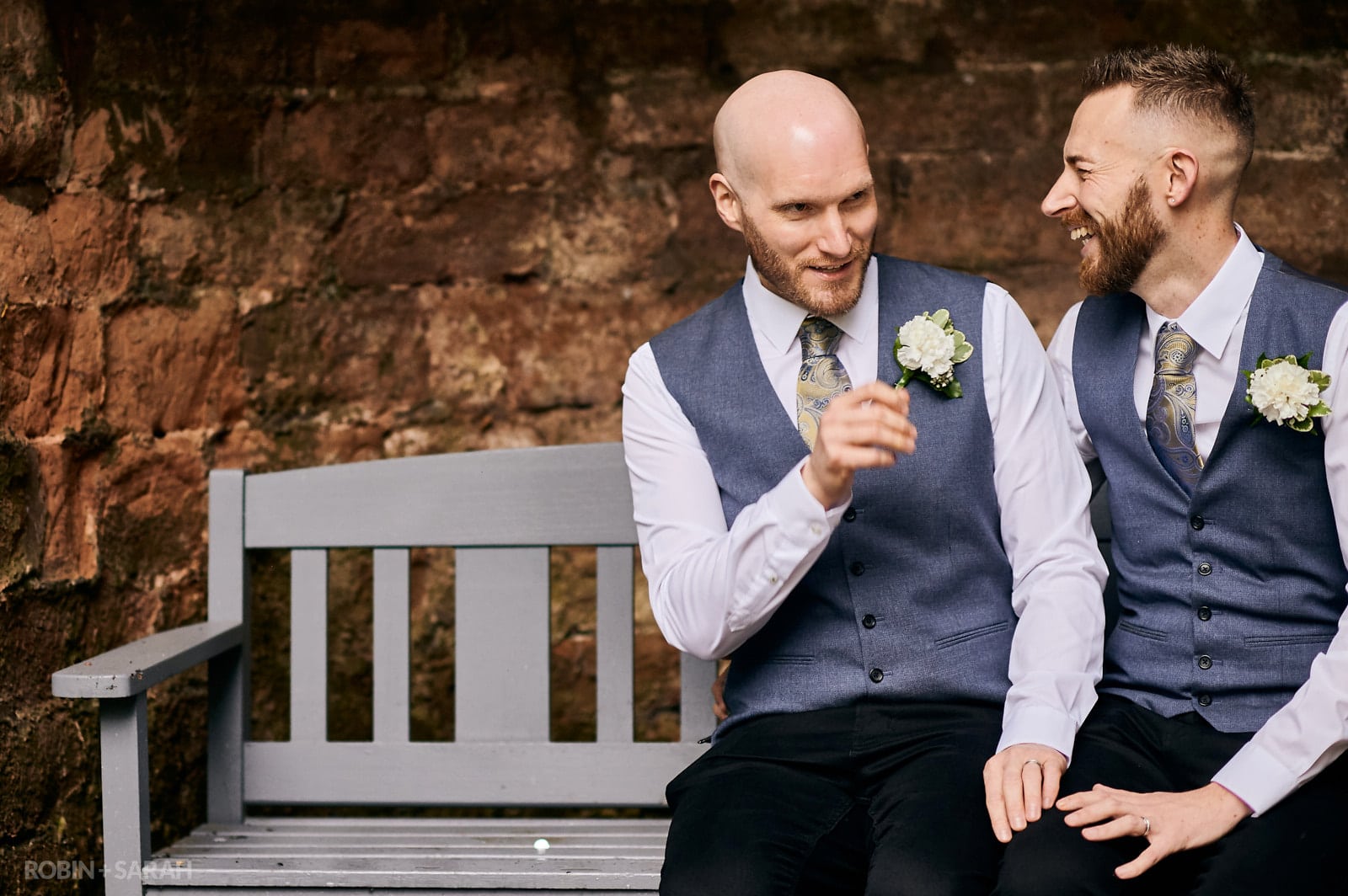Two grooms laughing as they sit together on bench