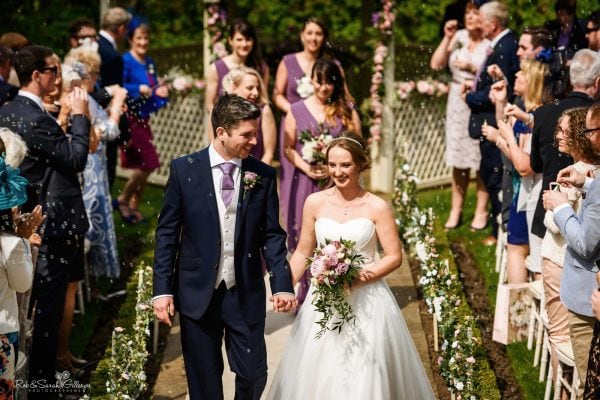 Bride and groom leave outdoor wedding ceremony as guests blow bubbles