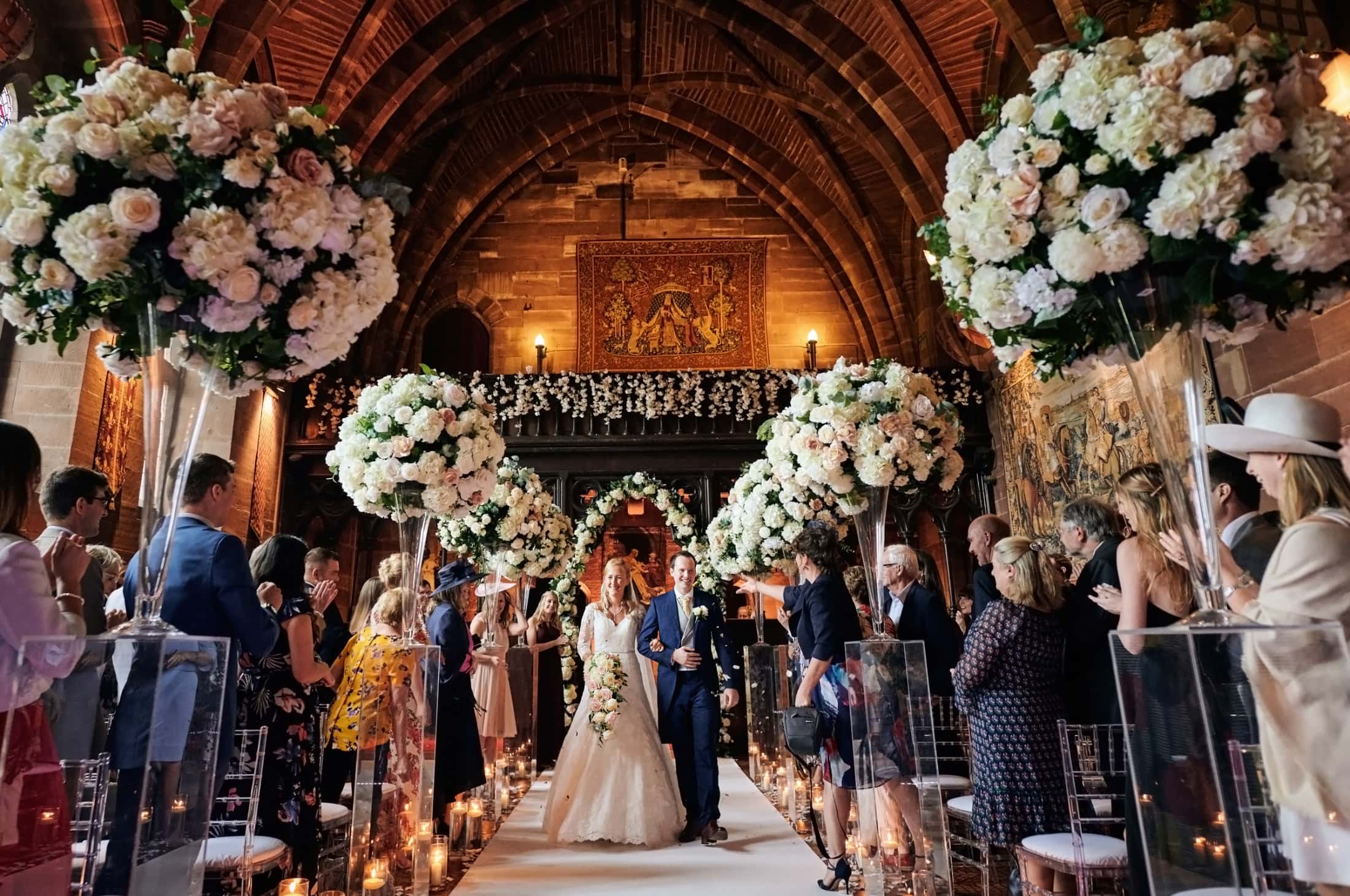 Bride and groom walk as wedding guests throw confetti in beautiful old hall
