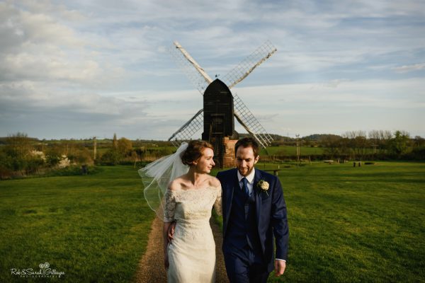 Bride and groom walking away from old windmill at Avoncroft Museum