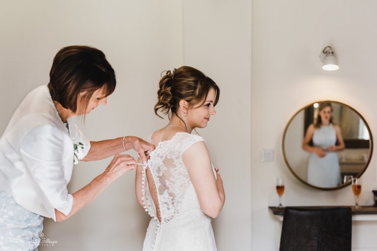 Bride has wedding dress fastened by mum while sister waits