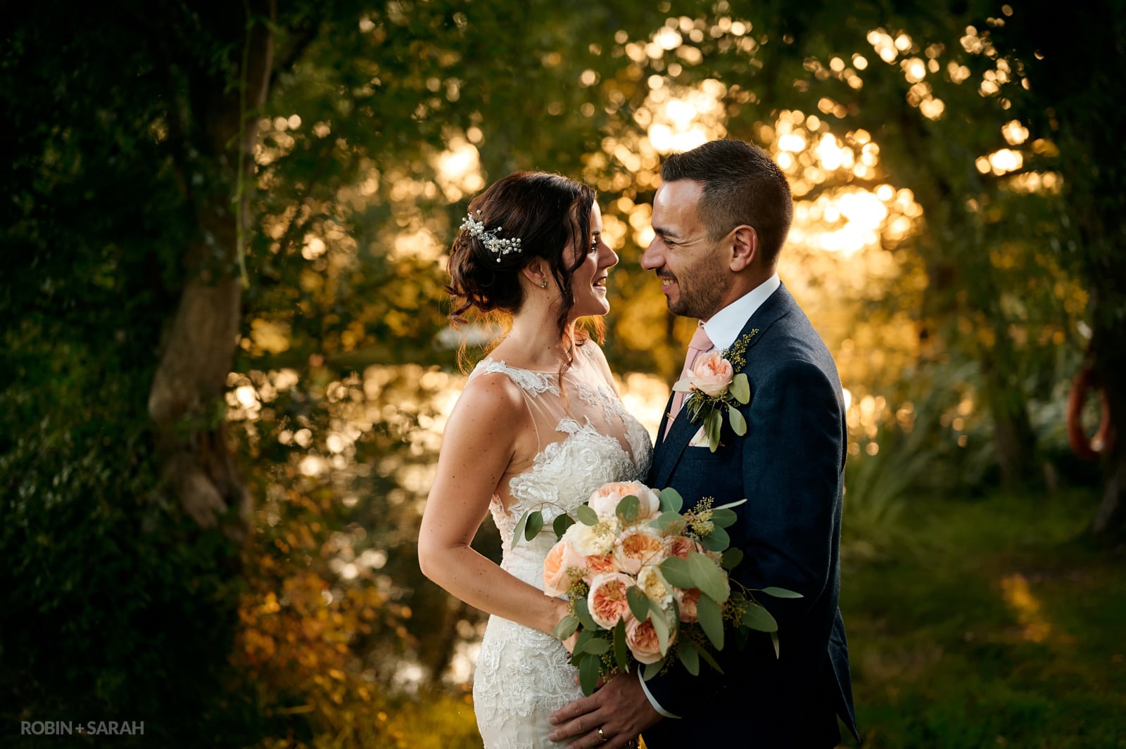 Bride and groom facing each other with beautiful sunset filtering through trees