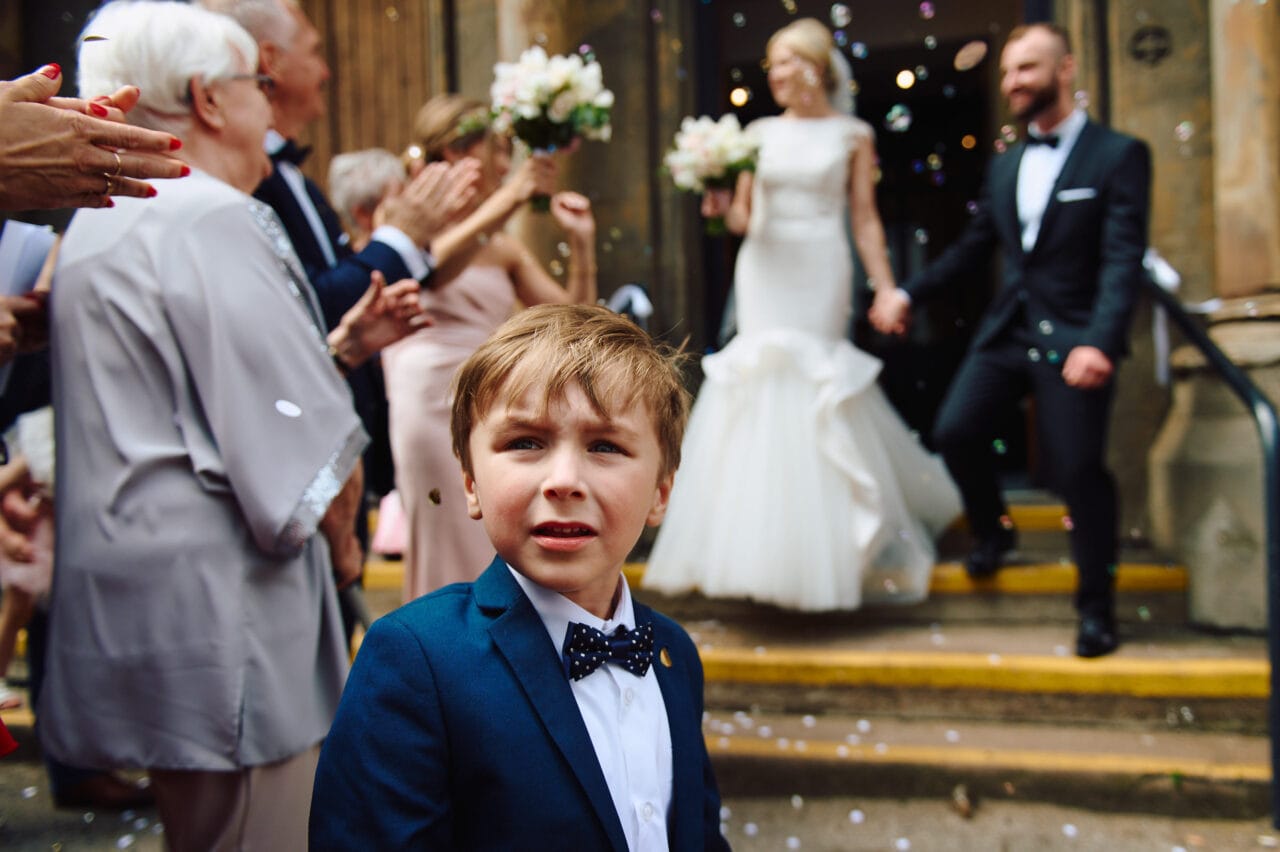 Pageboy turns to look as bride and groom have confetti throwing