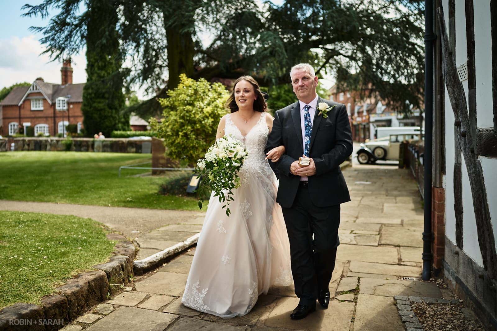 Bride and dad walk up pathway to church