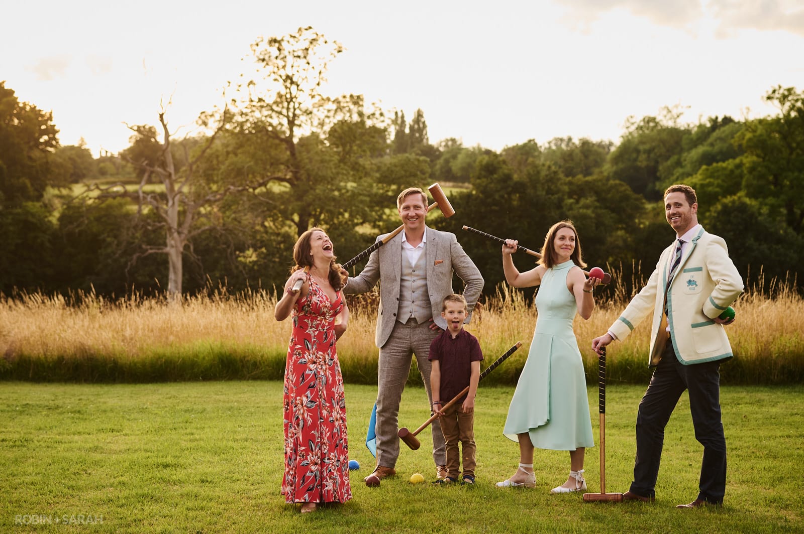 Wedding guests strike a pose with croquet mallets as sun sets behind them