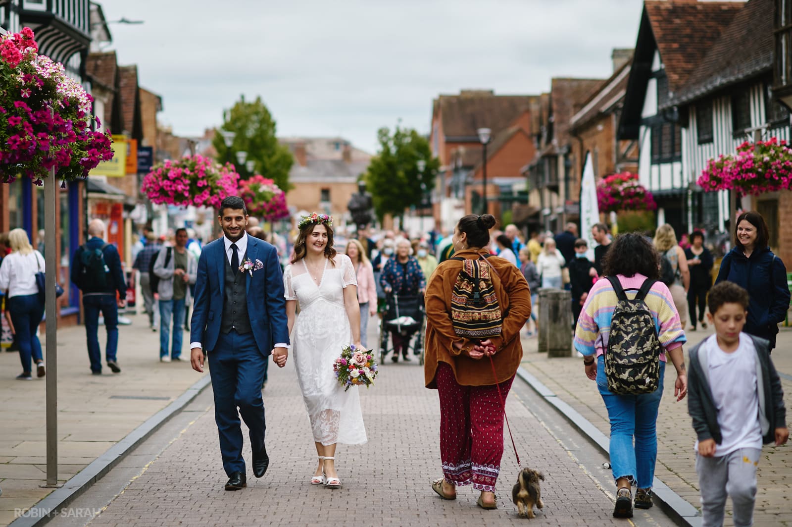 Bride and groom walk hand in hand through busy streets