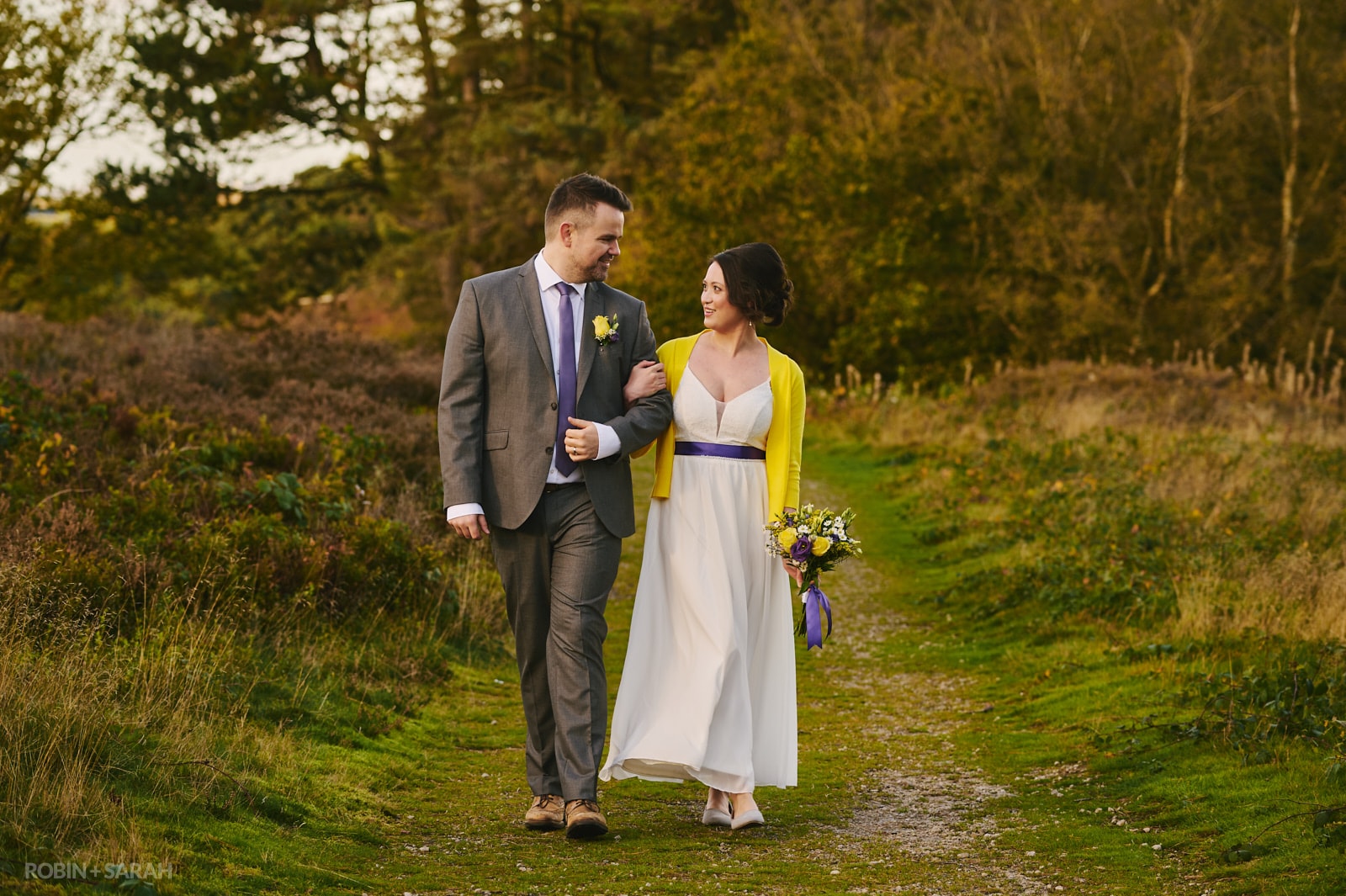 Bride in long dress with yellow cardigan and purple details walk together