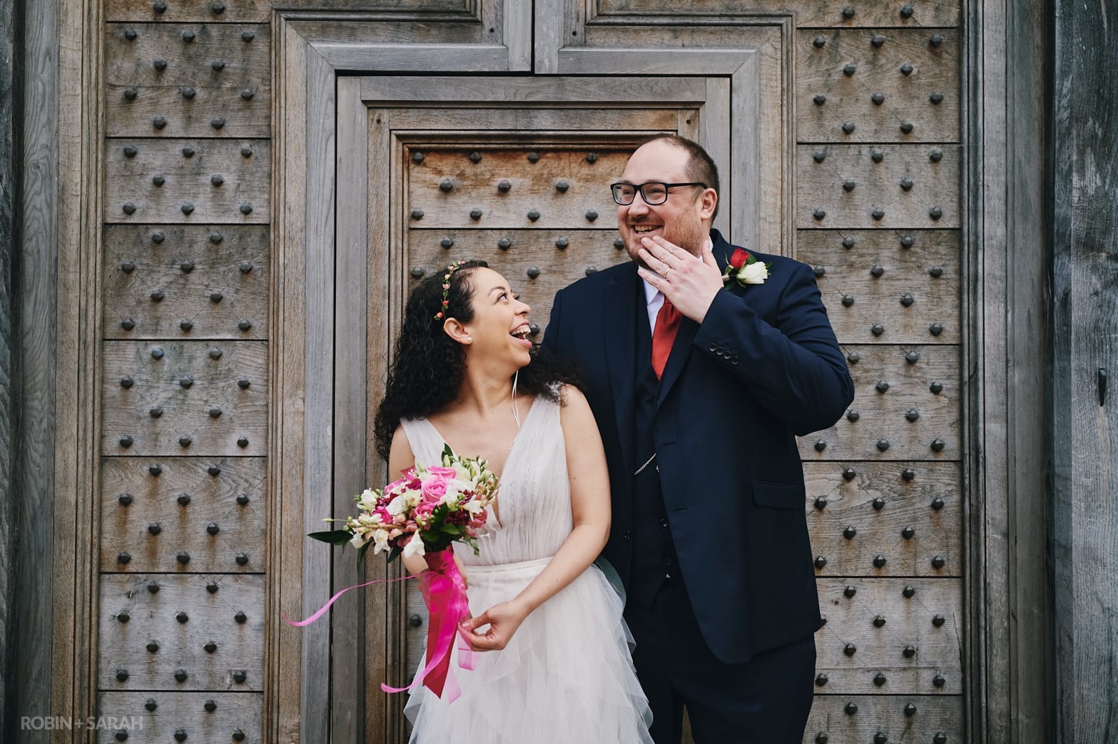 Bride and groom laughing together in front of old wooden doorway