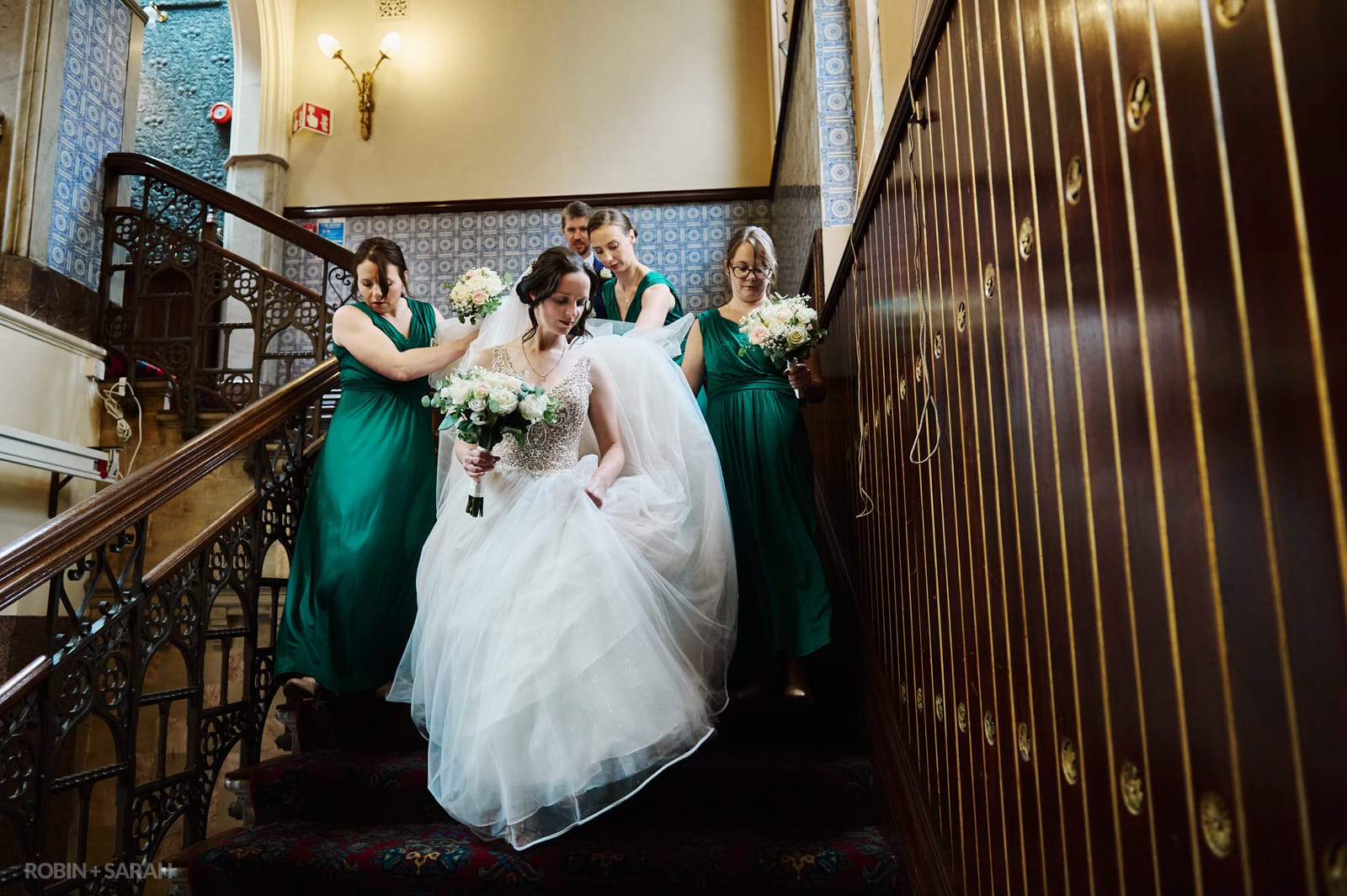 Bride and bridesmaids carefully walk down staircase