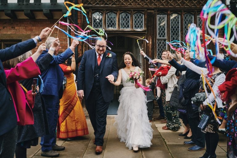 Bride and groom exit The Henley Room with guests waving colourful streamers