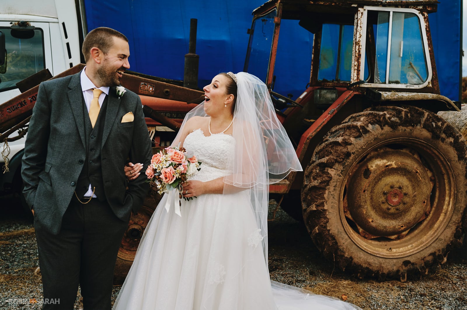 Bride and groom share a laugh in front of old tractor
