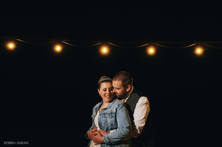 Bride and groom under festoon lights at night