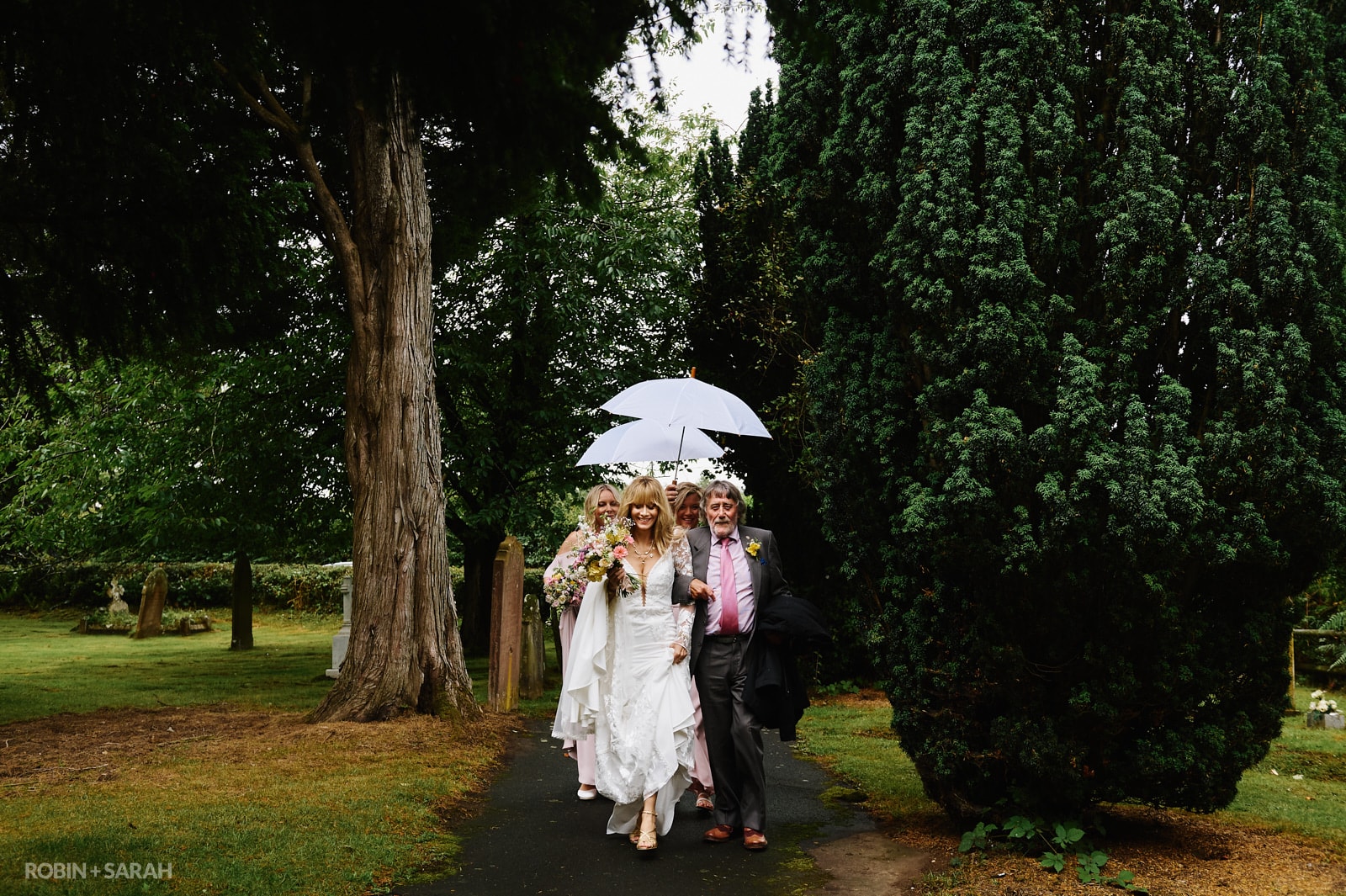 Bride, father and bridesmaids walk through churchyard