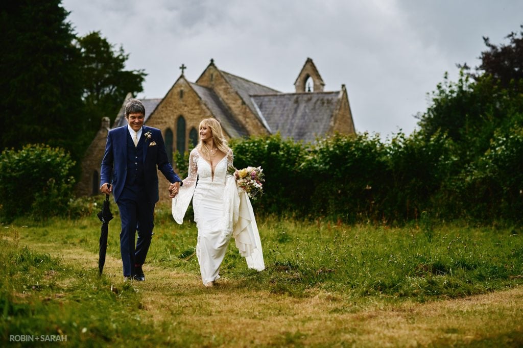 Bride and groom walk together outside Far Forest church in Worcestershire