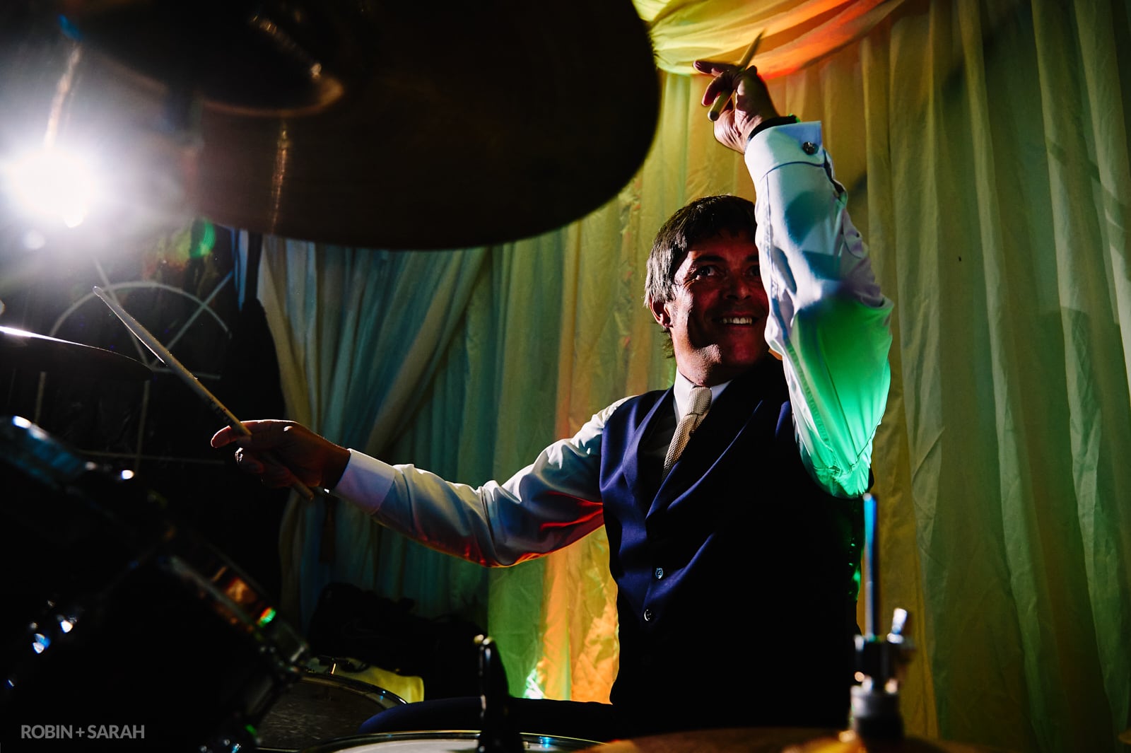 Groom plays drums with band in marquee wedding