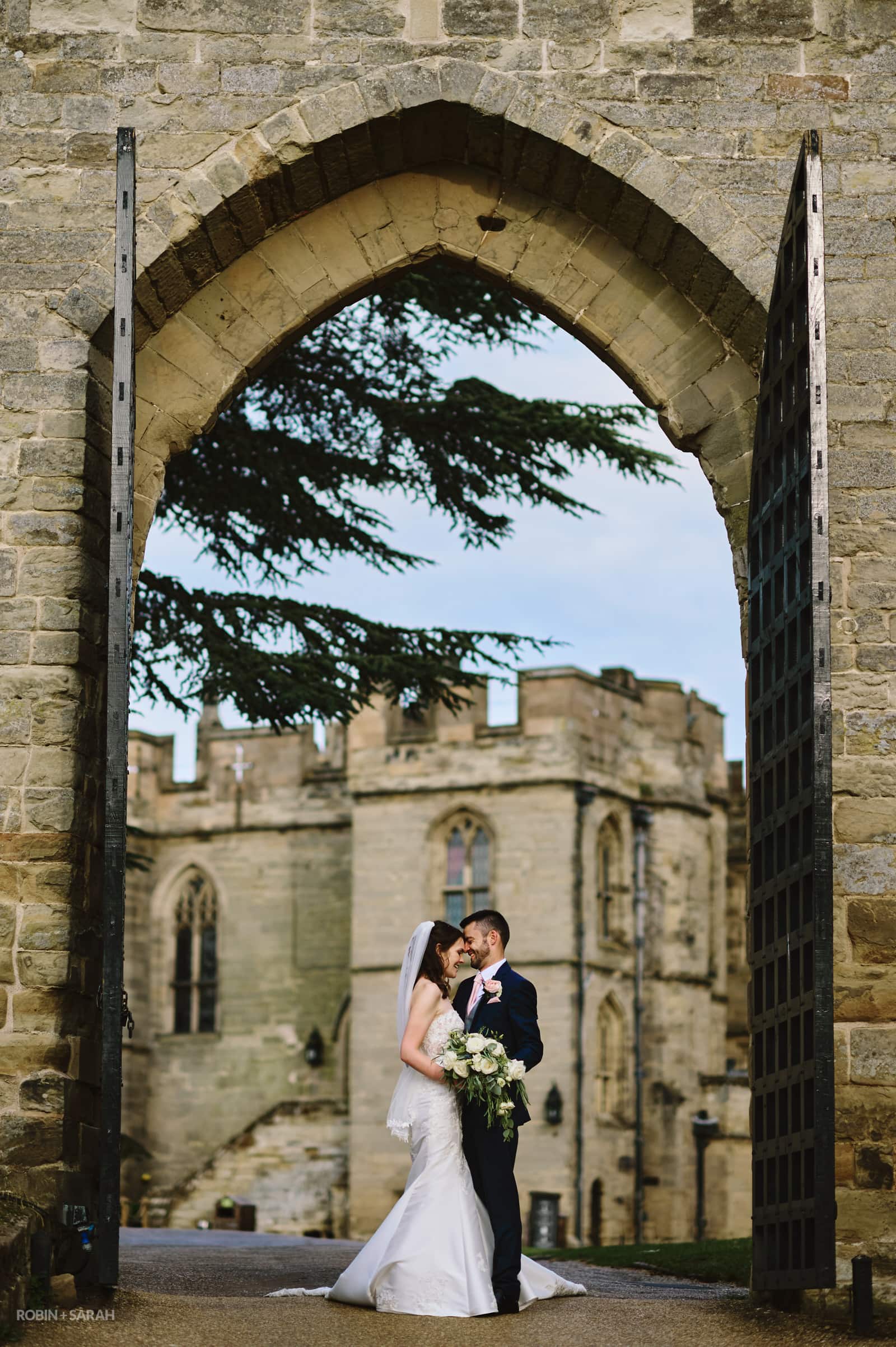Newly married couple under large stone arch at Warwick Castle