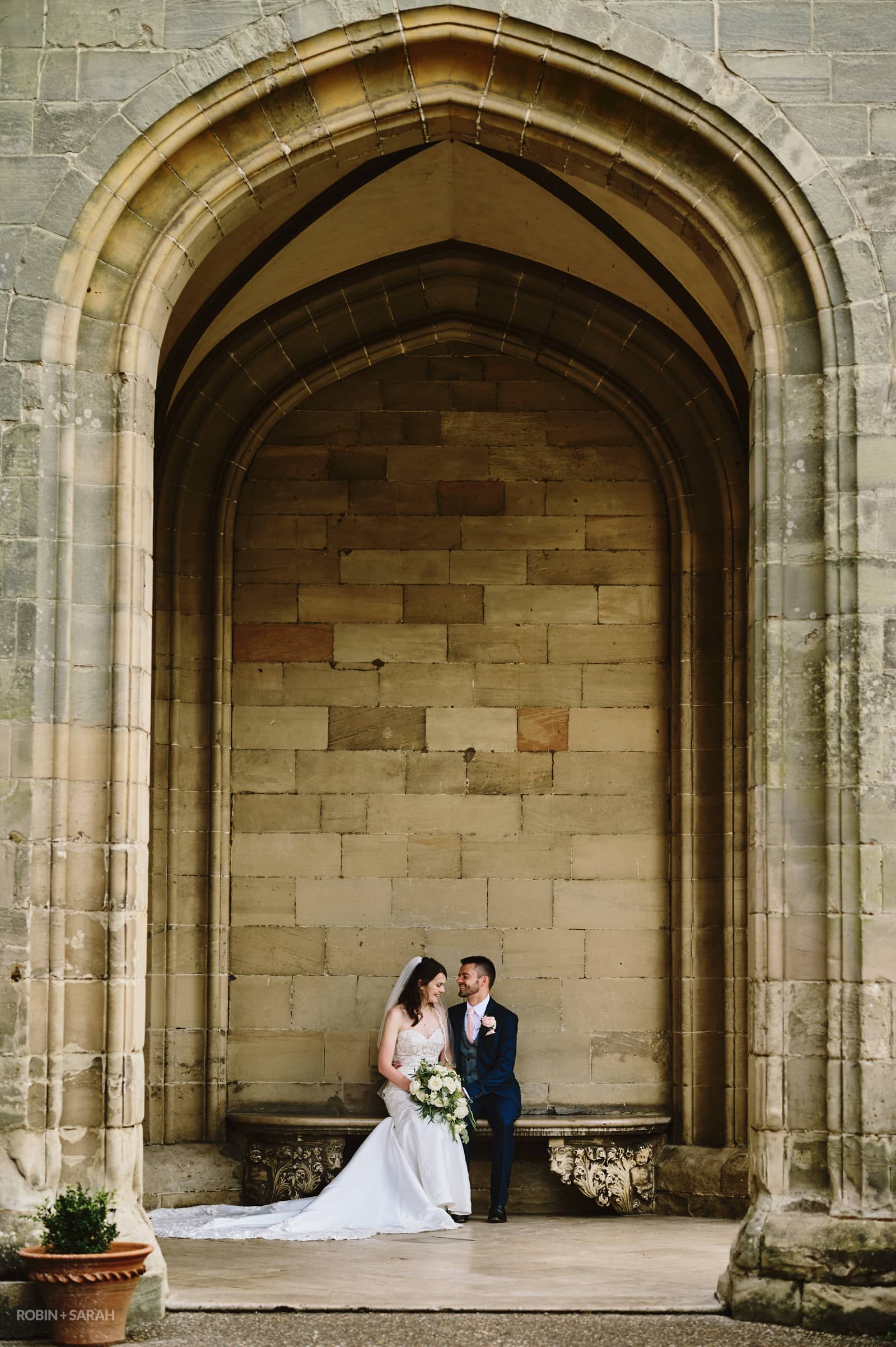 Bride and groom sit together under huge stone portico at Warwick Castle