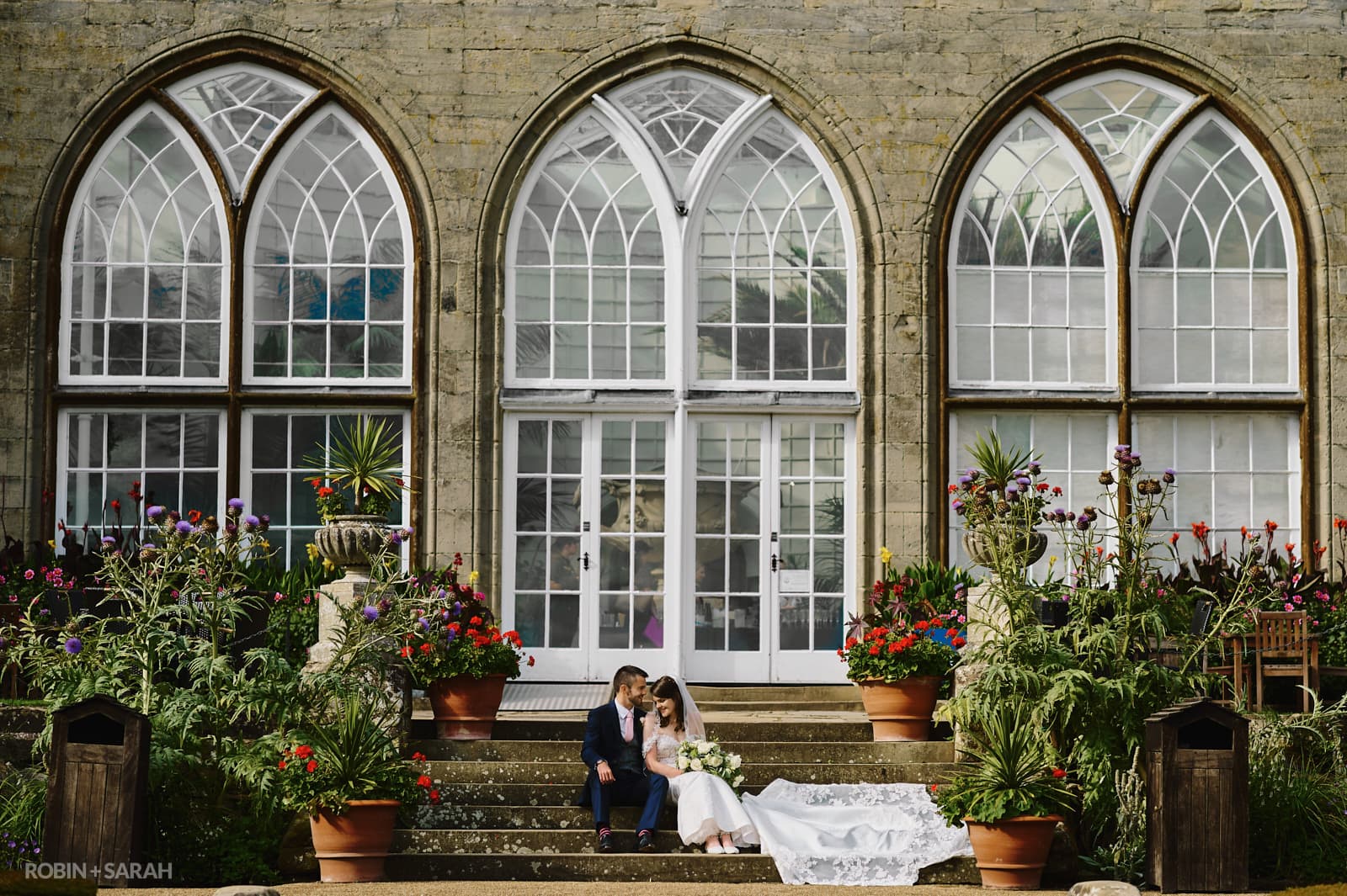Bride and groom sit on steps in front of The Conservatory building at Warwick Castle