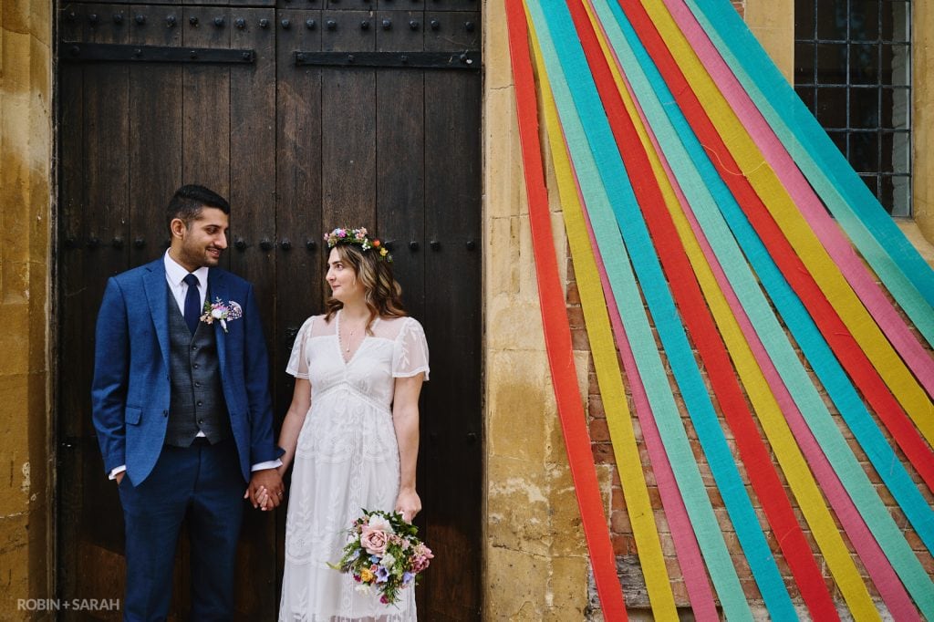 Bride and groom standing in doorway of old building with brightly coloured ribbons