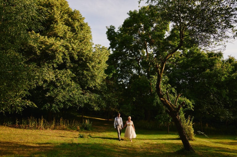 Bride and groom walk through beautiful trees at Oakfield Gardens
