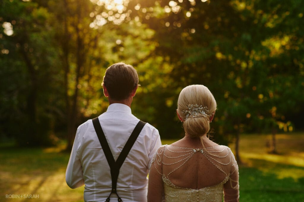 Back of bride and groom as they walk towards woods