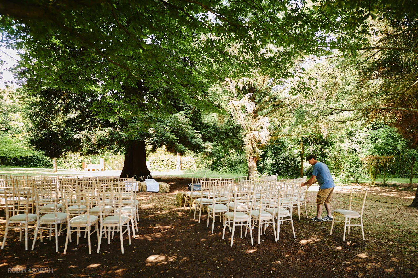 Groom sets out chairs for wedding ceremony under large tree