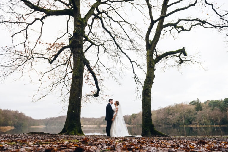 Bride and groom standing between two trees in shores of Bracebridge Pool in Sutton Coldfield