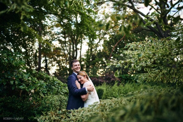 Bride and groom laughing together surrounded by trees in gardens at Moxhull Hall wedding