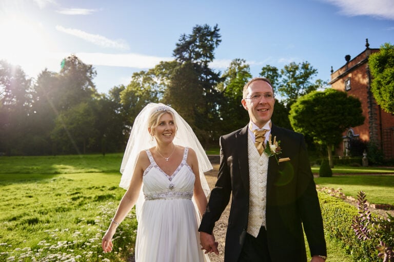 Bride and groom walk hand in hand through beautiful grounds at Staunton Harold