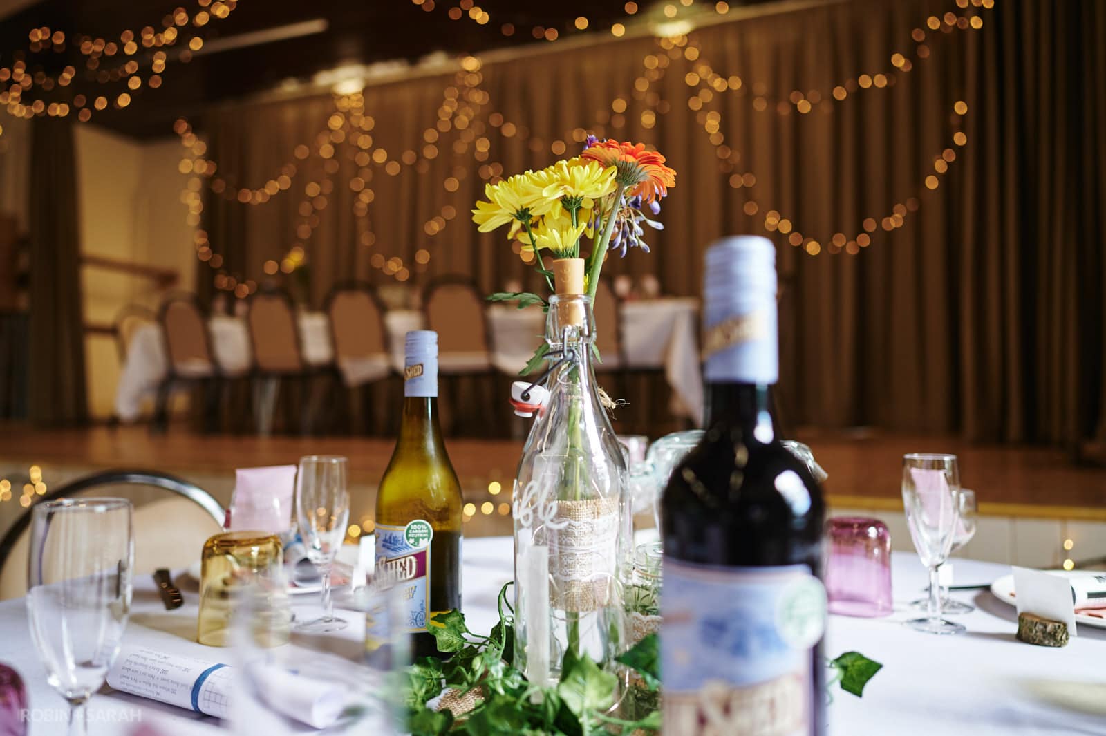Flowers and bottles of wine on table for wedding meal in village hall