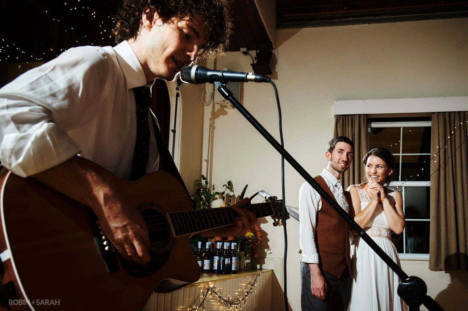 Bride watching her brother sing and play guitar at village hall wedding