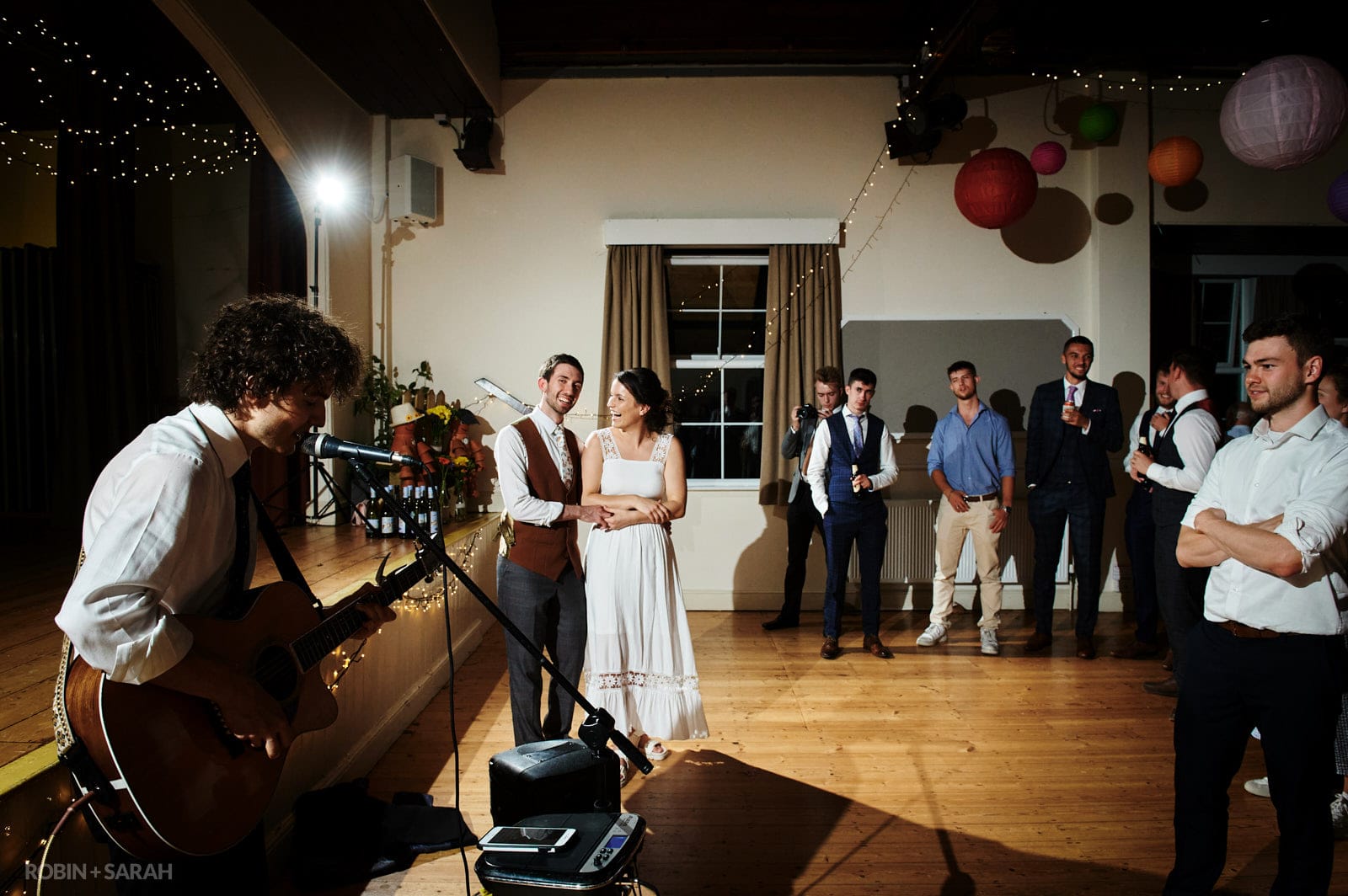 Bride and guests watch as musician performs live in village hall