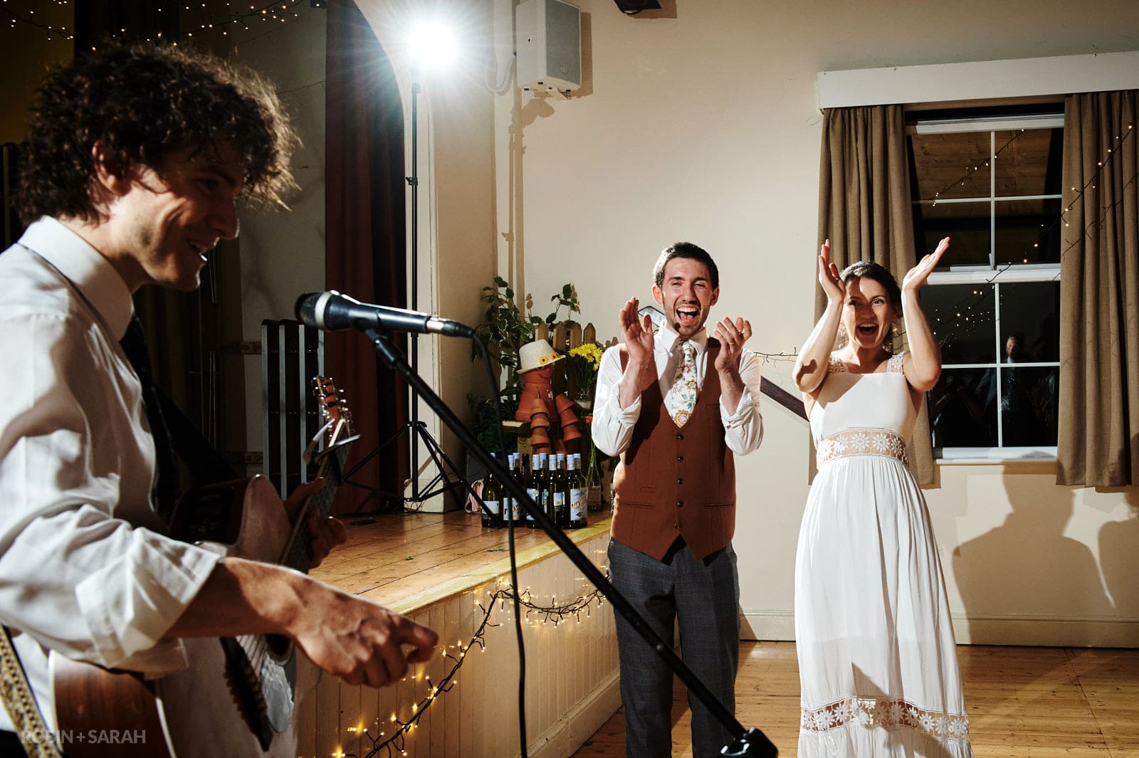 Bride and groom clap and cheer at live music performance at their wedding in village hall
