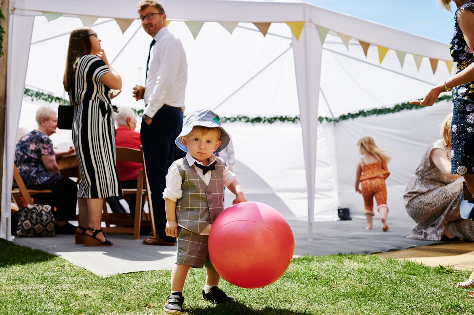 Young boy plays with red ball at DIY wedding party in garden
