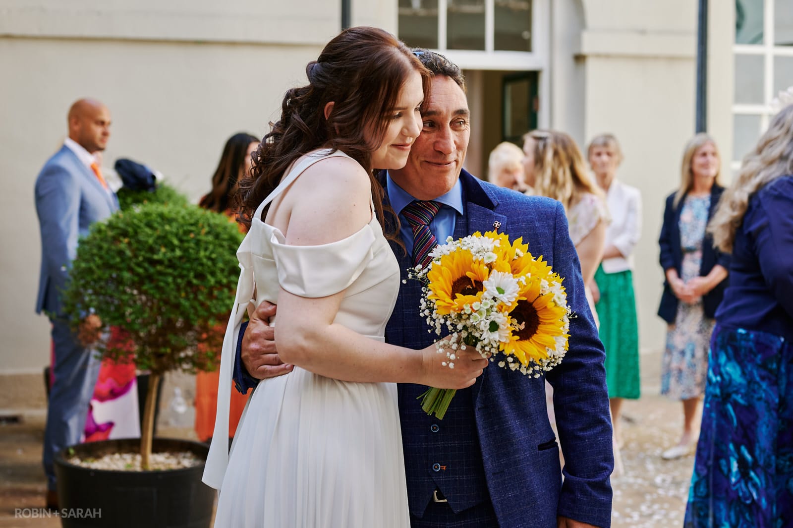 Bride hugged by her uncle in courtyard at Priory Place