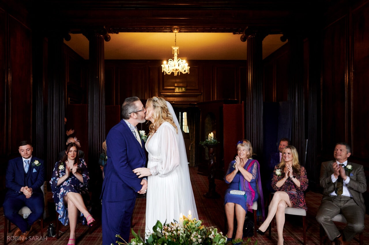 Bride and groom kiss at end of wedding ceremony in Walnut Room at Coombe Abbey