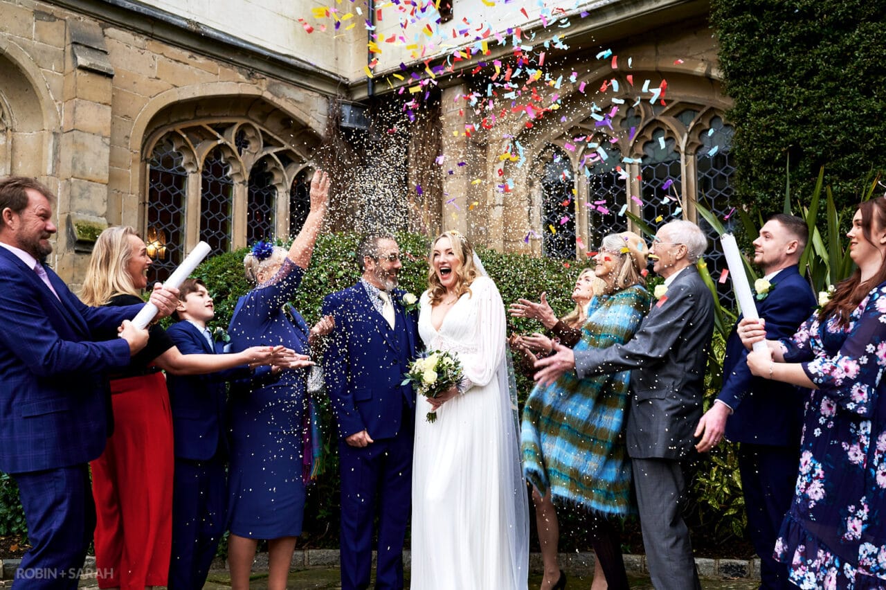 Small wedding party throw confetti over bride and groom in courtyard at Coombe Abbey