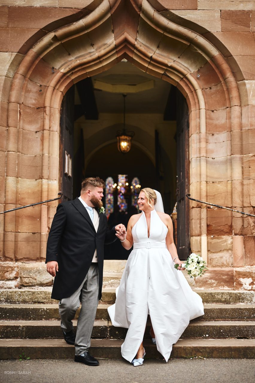 Newly married couple walk down steps at Hanbury Church in Worcestershire after wedding ceremony