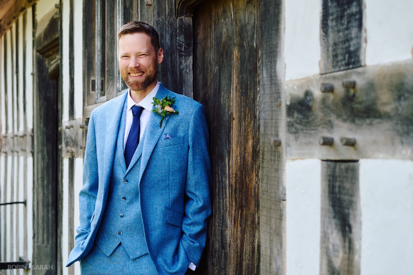 Portait of groom leaning against beautiful old half-timber building.