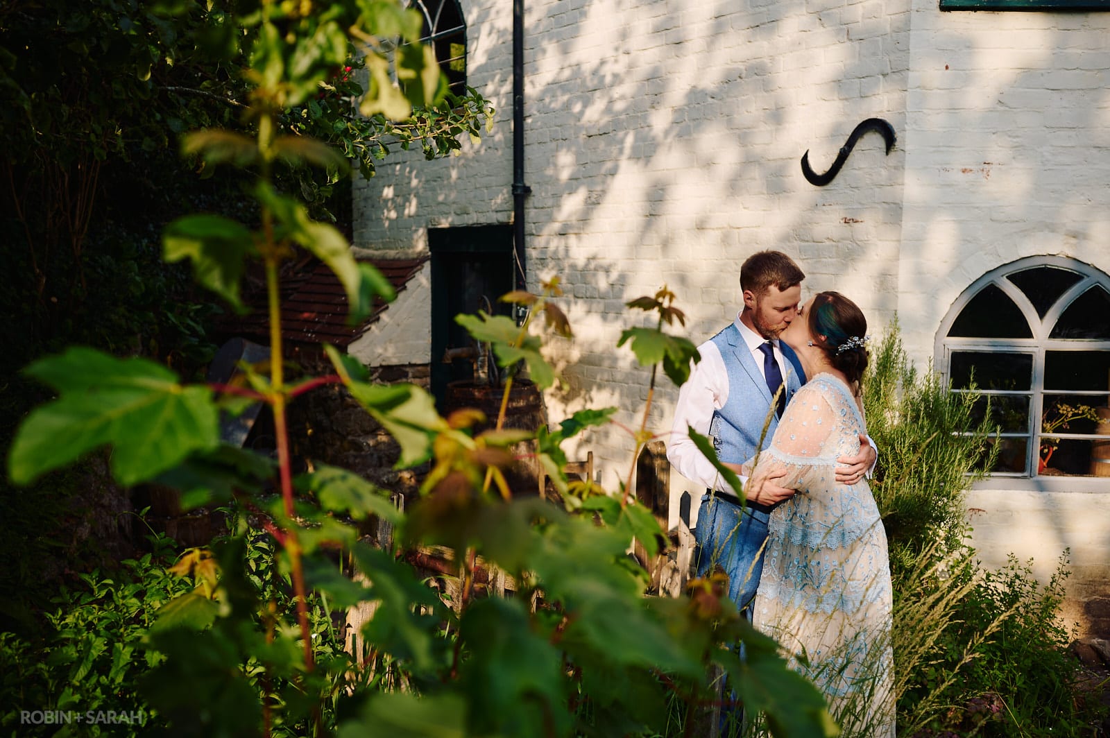 Bride and groom kiss in garden of old building